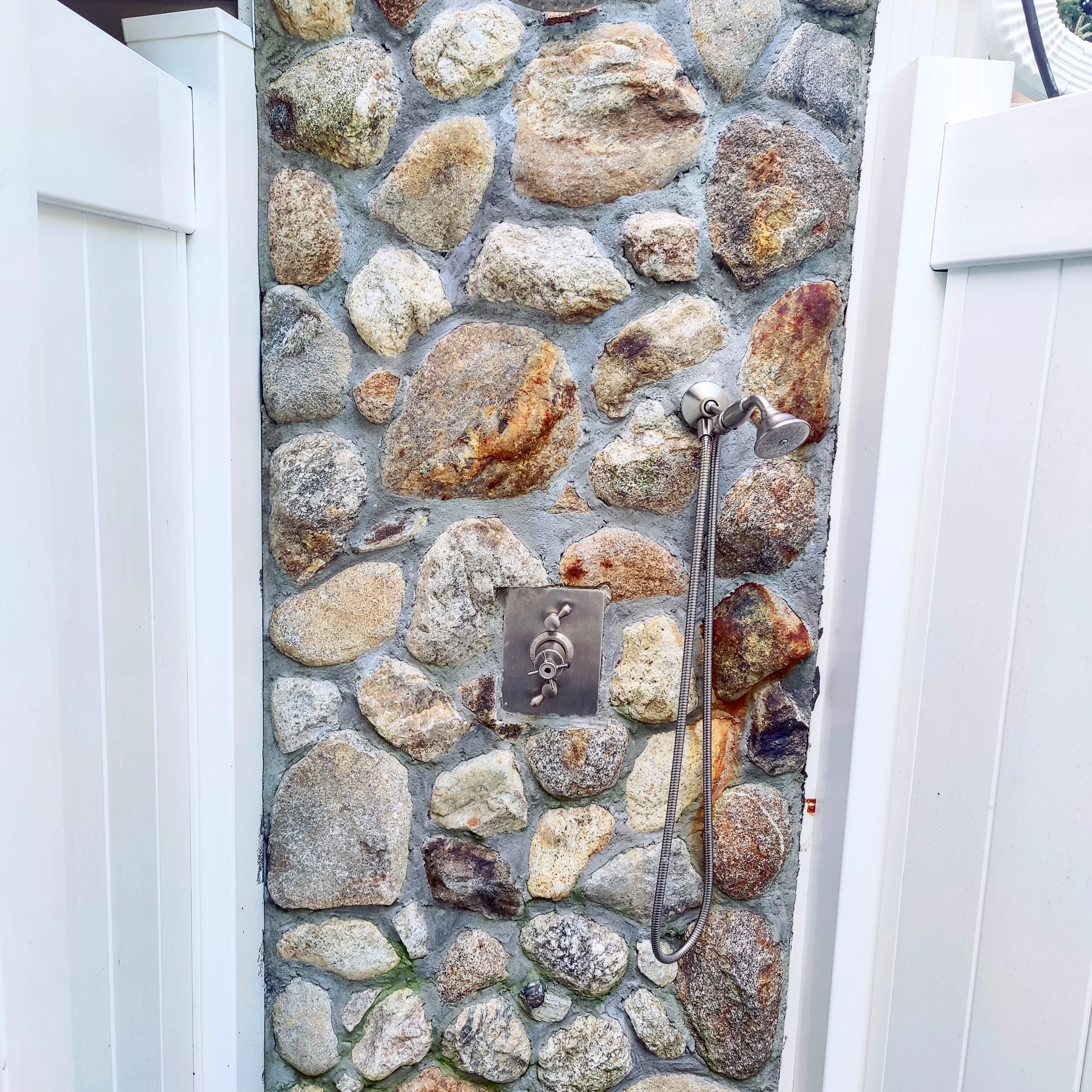 IMG_20210922_065538_470 A stone wall with a shower head and a white fence.